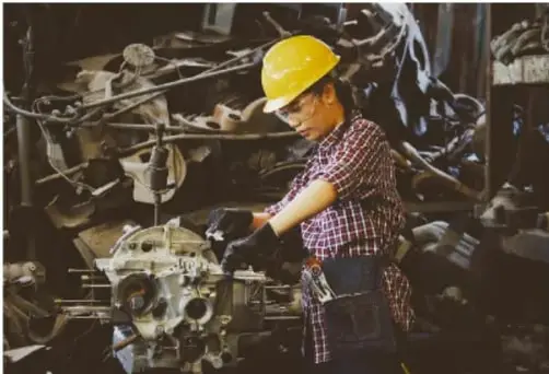 Fotografía de una persona con casco amarillo trabajando con herramientas en un taller mecánico, ilustrando el sistema técnico de arreglar un auto.