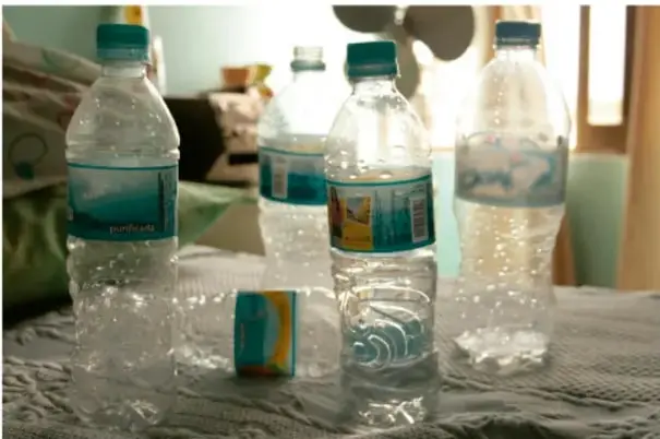 Botellas de plástico transparente con agua, algunas con etiquetas, colocadas sobre una mesa.