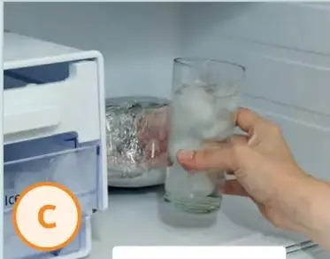Mano colocando un vaso C con hielo en el congelador.
