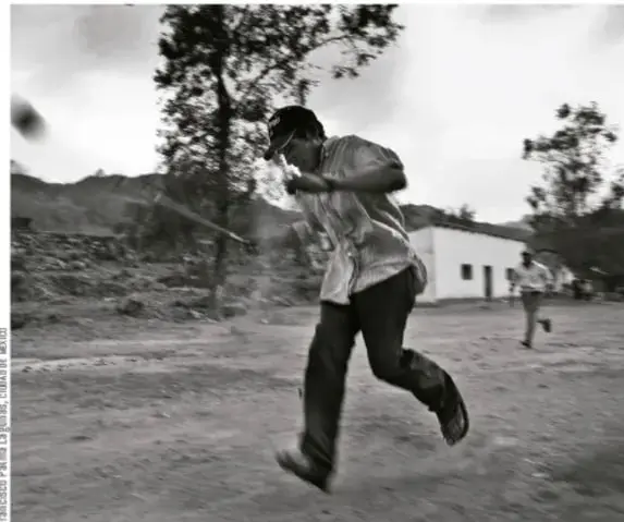 Fotografía en blanco y negro de un corredor ralámuli pateando la bola de madera durante el rarajipuami en un camino de la sierra; crédito a Francisco de la Luz / LUIS J. GARAY / VIVO.