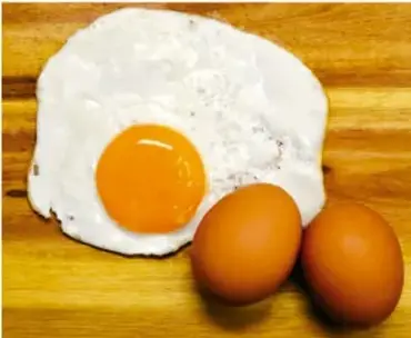 Fotografía de un huevo estrellado y dos huevos enteros sobre una superficie de madera, como ejemplo de alimento para el diario.