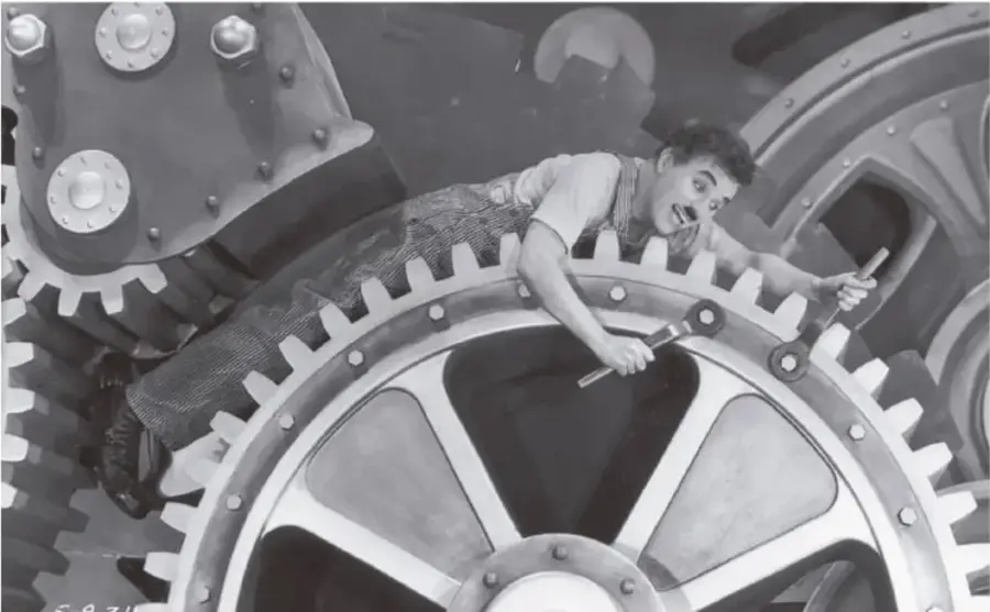 Fotograma en blanco y negro de la película Tiempos modernos (1936) de Charles Chaplin, mostrando al personaje del vagabundo atrapado entre los engranajes gigantes de una máquina industrial.