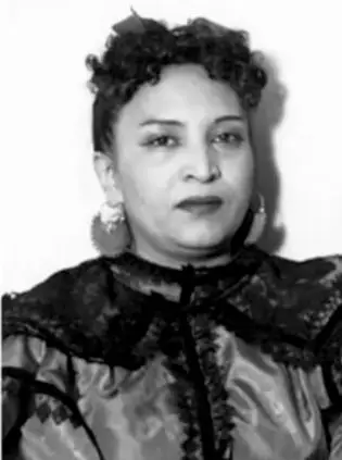 Retrato en blanco y negro de una mujer con cabello rizado, aretes grandes y vestido oscuro con encaje.