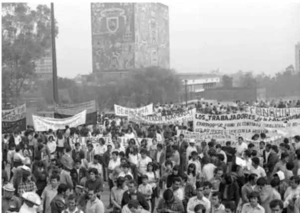 Fotografía en blanco y negro de una gran manifestación en la Plaza de las Tres Culturas, Tlatelolco, con maestros sosteniendo pancartas. Se lee 'LOS TRABAJADORES DE LA EDUCACIÓN' y 'DEMOCRACIA SINDICAL'.
