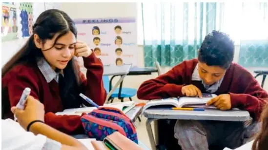 Fotografía de estudiantes de telesecundaria con uniforme rojo trabajando en su pupitre con libros y materiales escolares, en el aula.