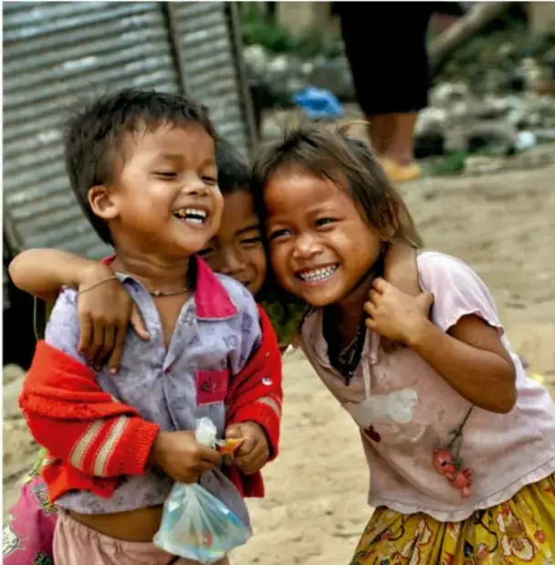 Fotografía de tres niñas sonriendo y abrazadas en un entorno de pobreza, ilustrando a la niñez vulnerable en comunidades marginadas.