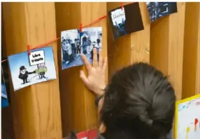 Estudiante de espaldas observando un tendedero de fotografías y mensajes de fotovoz colgados en un muro de madera.