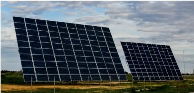 Fotografía de dos hileras de paneles solares fotovoltaicos inclinados en un campo, bajo cielo con nubes.