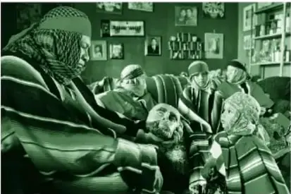 Fotografía (en tinta verde del libro) de cinco personas vestidas con sarapes coloridos y paliacates dentro de una casa; el señor sostiene y mira una máscara de parachico, un niño lo observa de pie y al fondo tres personas descansan en un sillón.