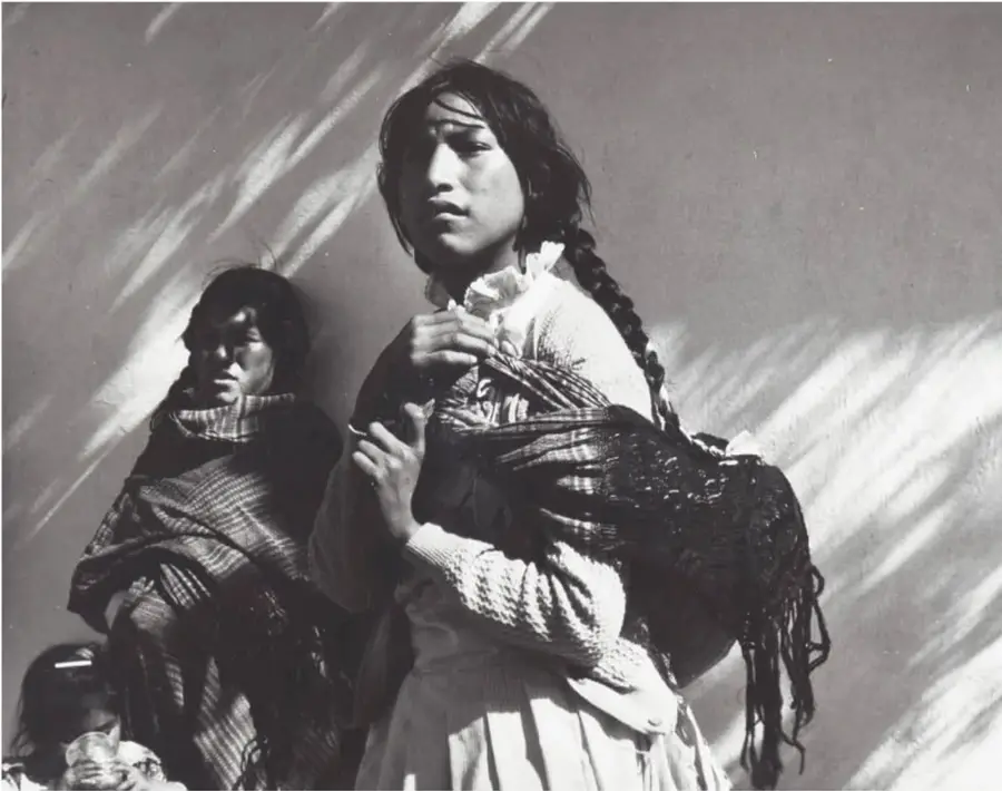 Fotografía en blanco y negro de mujeres mazahuas con rebozos y trenzas junto a una niña, iluminadas por luz de atardecer; Mujeres Mazahuas, 1989, Estado de México, de Mariana Yampolsky (1925-2002).