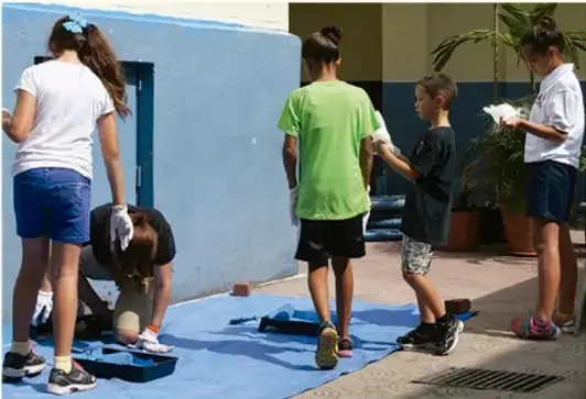 Fotografía de cinco estudiantes trabajando en equipo: pintan un muro azul y manipulan materiales durante una jornada de trabajo comunitario.