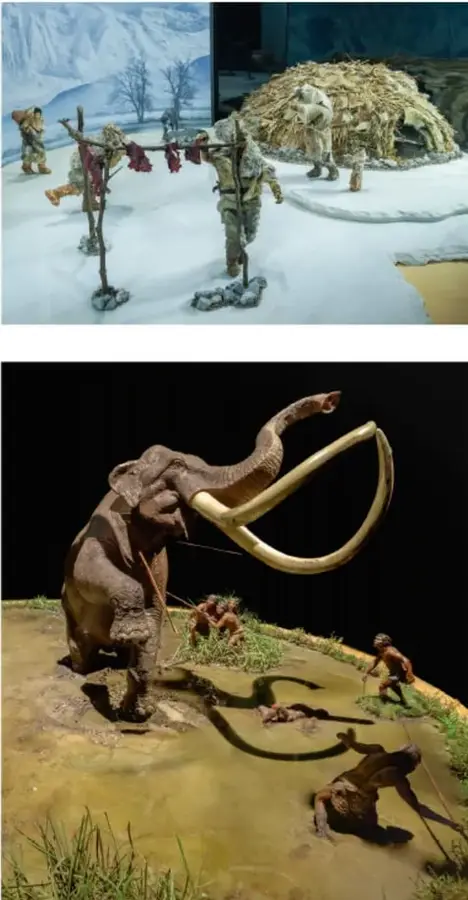 Diorama de un grupo de cazadores-recolectores nómadas con vestimenta de pieles, lanzas y un refugio de ramas en un paisaje nevado.