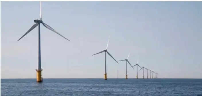 Fotografía de un parque eólico marino: fila de aerogeneradores instalados sobre el mar, con sus bases ancladas en el agua y las hélices en el cielo.