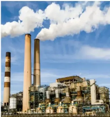 Fotografía de una central térmica o planta industrial con grandes chimeneas que emiten humo, bajo un cielo azul con nubes; ilustra la contaminación derivada de la actividad industrial.