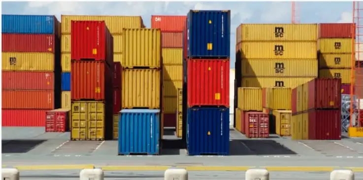 Fotografía de contenedores de carga apilados en un puerto, en colores rojo, azul y amarillo, símbolo del comercio internacional y la globalización.