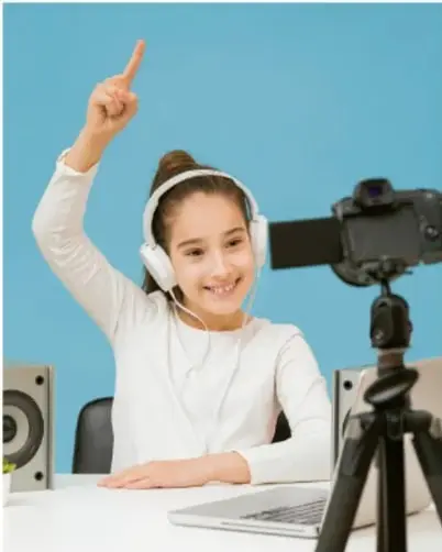 Fotografía de una joven con audífonos y laptop frente a una cámara en trípode, levantando un dedo señalando, ilustrando la creación de contenido audiovisual.