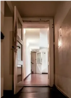 Fotografía de una puerta abierta que deja ver un pasillo iluminado con escaleras al fondo.