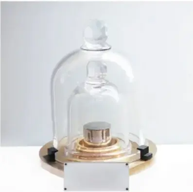 Fotografía del patrón internacional del kilogramo: un cilindro metálico de iridio y platino protegido por dos campanas de vidrio sobre una base circular.