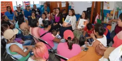 Reunión comunitaria con personas sentadas en círculo, algunas con carteles, en un espacio abierto.