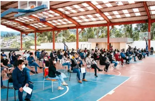 Fotografía de un grupo de estudiantes reunidos en un patio o cancha techada, sentados en sillas ordenadas, participando en una actividad comunitaria escolar.