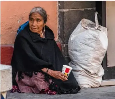 Mujer indígena adulta sentada en la calle junto a un costal, con una taza, en aparente situación de mendicidad.