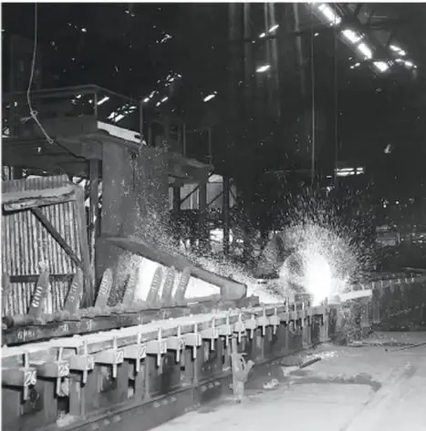 Fotografía en blanco y negro de una planta industrial con maquinaria pesada y chispas, que ilustra el auge industrial de la época.