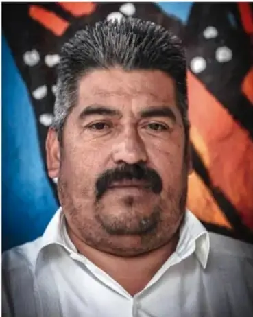 Fotografía de Homero Gómez González, hombre con bigote y camisa blanca, frente a un fondo colorido.