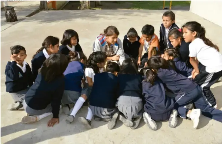 Fotografía de un grupo de estudiantes de primaria sentados en círculo en el patio de la escuela, dialogando y tomando acuerdos.