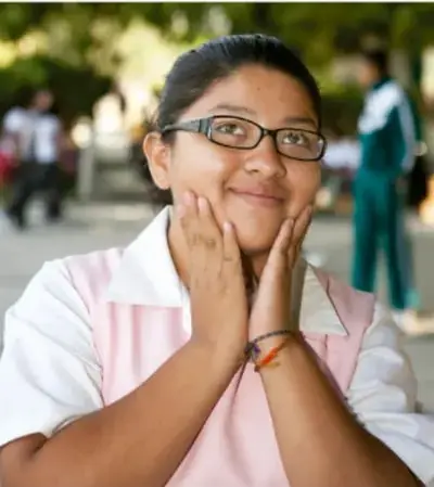 Fotografía de una estudiante de Telesecundaria con lentes, sonriente, con las manos en el rostro; crédito: Francisco Manuel Palma Lagunas, Ciudad de México.