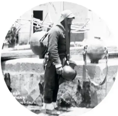 Persona de espaldas cargando cántaros o tinajas sujetos con un mecapal que pasa por su frente, junto a una pila o fuente de agua.