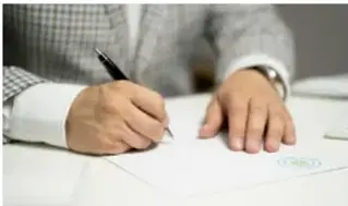 Manos de una persona firmando un documento con pluma sobre un escritorio, ilustrando acuerdos formales basados en leyes.
