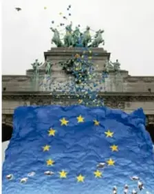 Ilustración de un edificio europeo con una bandera de la Unión Europea (fondo azul con estrellas amarillas) y estatuas en su parte superior, símbolo del nuevo orden mundial europeo.