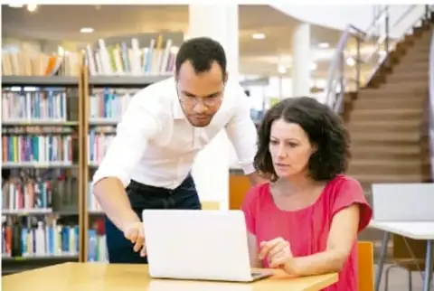 Dos personas trabajando con una laptop en una biblioteca.