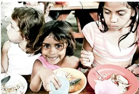 Fotografía de tres niñas comiendo alimentos en la escuela, ilustrando el derecho a la alimentación nutritiva.