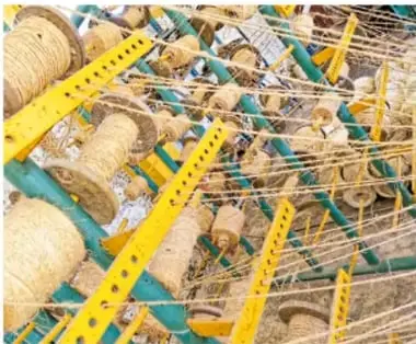 Mesa con artesanías de fibra de henequén teñida de colores, como figuras y bolsas pequeñas, en un mercado.