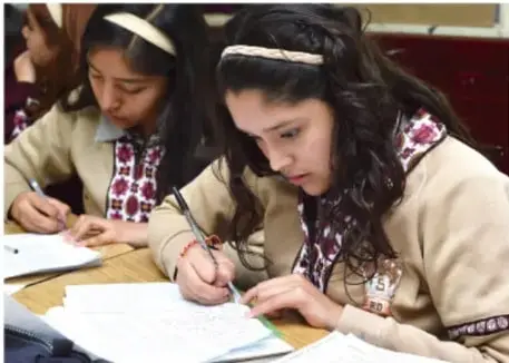 Dos estudiantes de secundaria con cabello largo escriben en sus cuadernos durante una actividad de indagación en el aula.