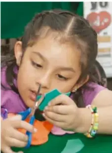 Karina, niña pequeña que realiza una manualidad con tijeras y papel de color.