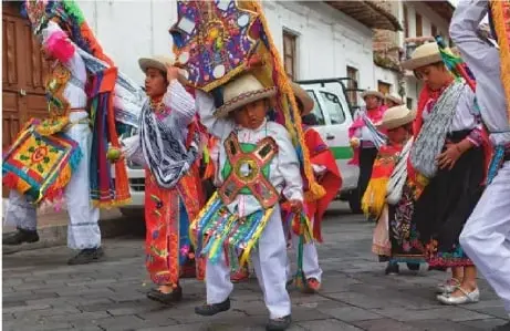 Niños, niñas y personas adultas participan en una celebración cultural y religiosa con vestimenta tradicional.