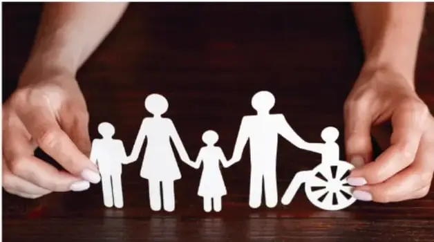 Manos sosteniendo recortes de papel de una familia con figuras de niños, adultos y una persona en silla de ruedas, simbolizando diversidad e inclusión.