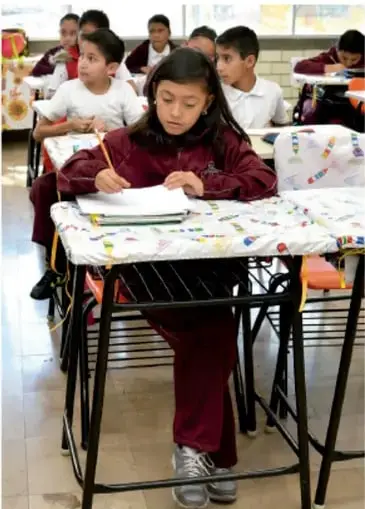 Estudiantes de primaria sentados en sus pupitres escribiendo en el aula.