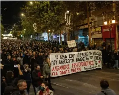 Multitud en una protesta nocturna con pancartas en griego, relacionada con la crisis económica.