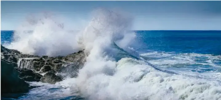 Fotografía de olas rompiendo con fuerza sobre las rocas, representando el movimiento de las mareas.