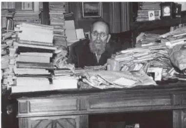 Fotografía en blanco y negro de un historiador sentado ante su escritorio, rodeado de numerosos libros y papeles.