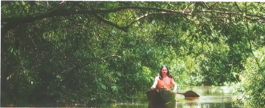Fotografía de una persona navegando en una canoa por un río rodeado de vegetación de la selva amazónica.