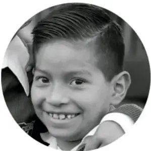 Fotografía en blanco y negro de un niño sonriente con camisa, mirando a la cámara.