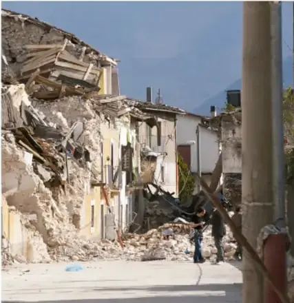 Fotografía de edificios dañados o en ruinas tras un desastre, con escombros en la calle.