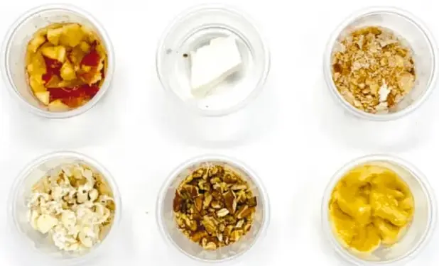 Seis vasos pequeños con muestras de alimentos: manzana, queso, avena, palomitas, granola y mango.