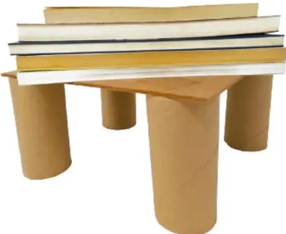 Mesa pequeña hecha con cuatro tubos de cartón gruesos como patas y una tabla encima, con libros apilados sobre ella.