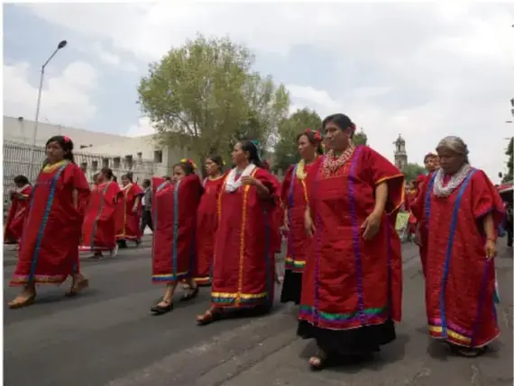 Fotografía de un grupo de mujeres indígenas con vestimenta tradicional roja caminando en una marcha o celebración.