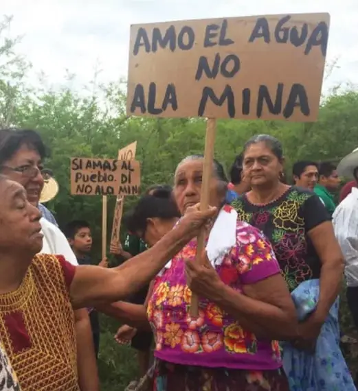 Fotografía de una protesta con personas sosteniendo carteles que dicen 'AMO EL AGUA NO A LA MINA' y 'SI AMAS AL PUEBLO DI NO A LA MINA'.